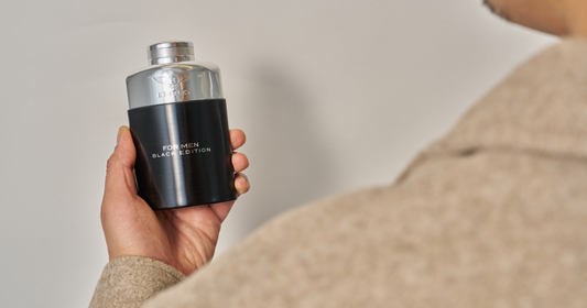 A man in a brown jacket holding a bottle of Bentley for Men Black Edition Eau de Toilette.