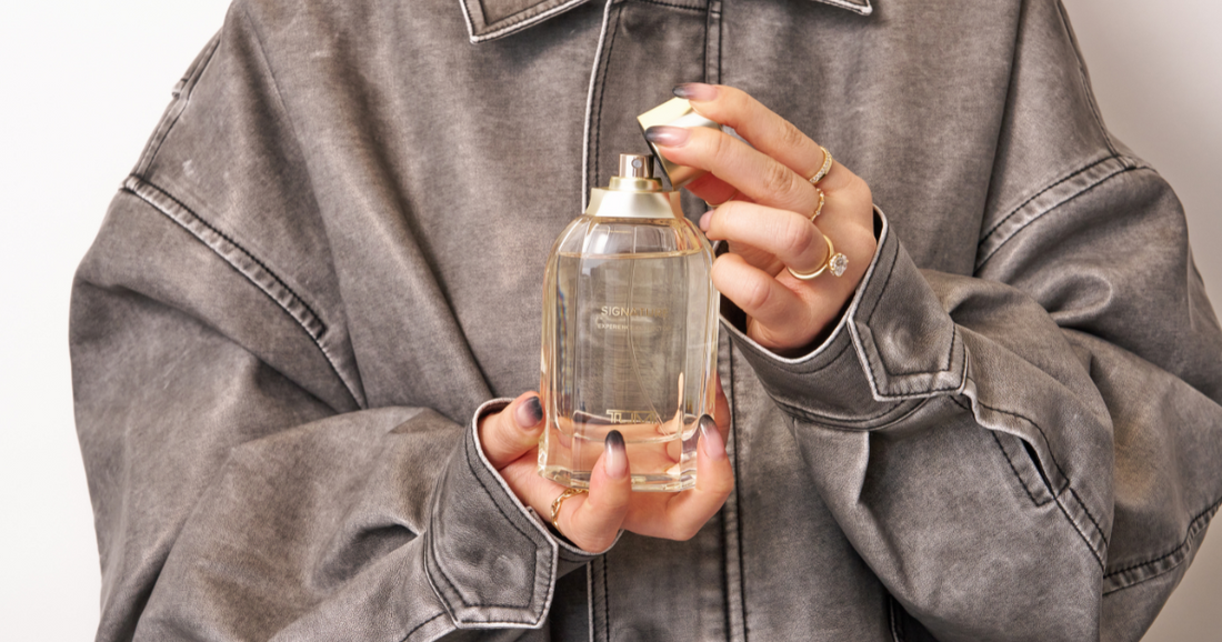 A woman in a grey jacket holding a bottle of perfume.