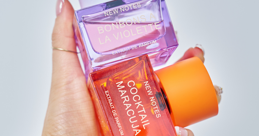 A woman's hand holding a bottle of NEW NOTES Cocktail Maracuja Extrait de Parfum and Bonbons A La Violette Extrait de Parfum.