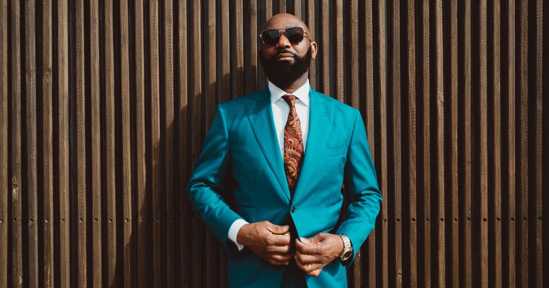 A man in a blue suit wearing sunglasses against a brown wall.