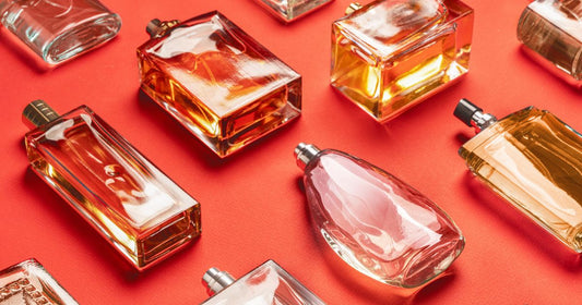 Various fragrance bottles of different notes laying on their side against a deep orange background.