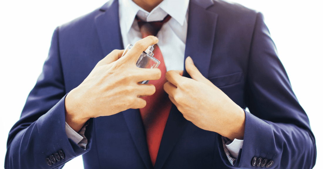 A man wearing a suit sprays cologne on his shirt.
