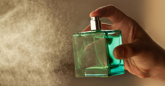 A man holds a green perfume bottle and sprays it into the air.