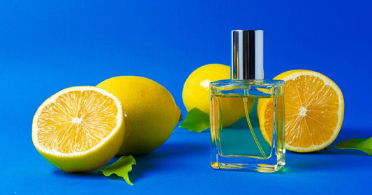 A bottle of lemon perfume or cologne with cut lemons against a bright blue background.