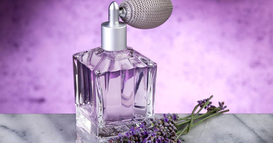 A bottle of lavendar perfume on a marble counter against a purple background next to some lavendar.