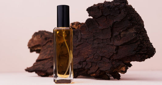 A bottle of sandalwood fragrance with bark against a pink background.
