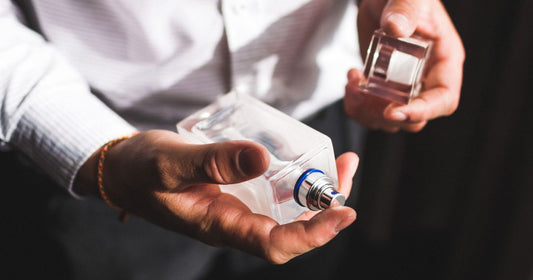 A man in a button down shirt holding a cologne bottle.