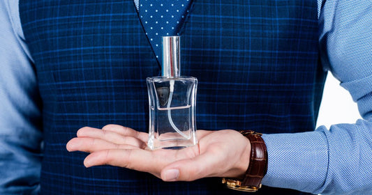 A man wearing a blue suit holding a cologne bottle in his hand.