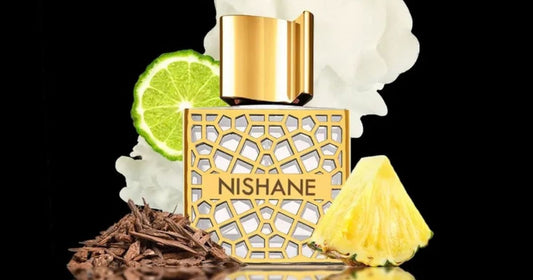 A Nishane fragrance bottle against a black background surrounded by pineapple, lime and other ingredients.