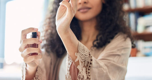 A woman in a fancy robe sprays perfume on her wrist.